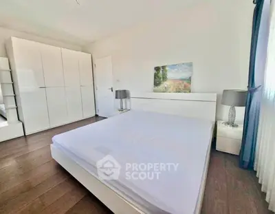 Spacious bedroom with modern white furniture and natural light, perfect for relaxation.