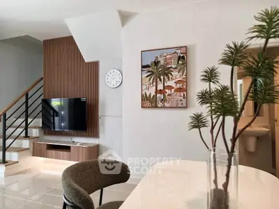 Modern living room with stylish decor and staircase, featuring a wall-mounted TV and elegant furniture.