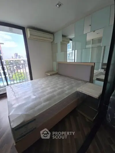 Modern bedroom with mirrored wall and city view balcony in high-rise apartment.