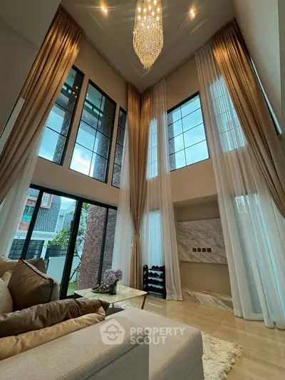Luxurious high-ceiling living room with elegant chandelier and large windows
