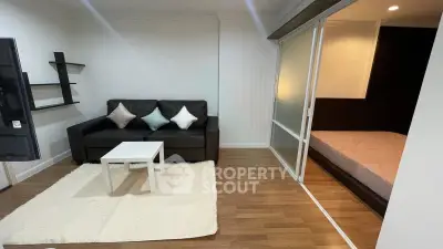 Modern living room with sleek black sofa and cozy bedroom separated by sliding glass doors.