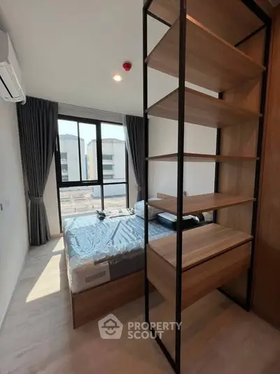 Modern bedroom with large window and stylish shelving unit, offering ample natural light and contemporary design.