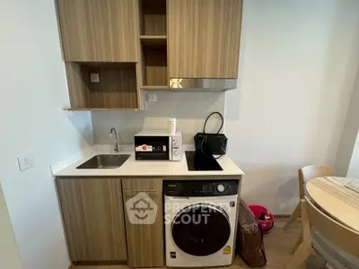 Modern compact kitchen with wooden cabinets, washing machine, and dining area in cozy apartment.
