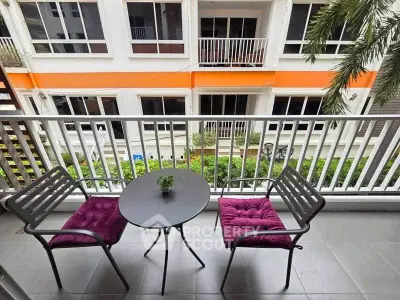 Charming balcony with cozy seating overlooking lush greenery in modern apartment complex.