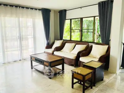 Spacious living room with elegant wicker furniture and large windows offering lush garden views.