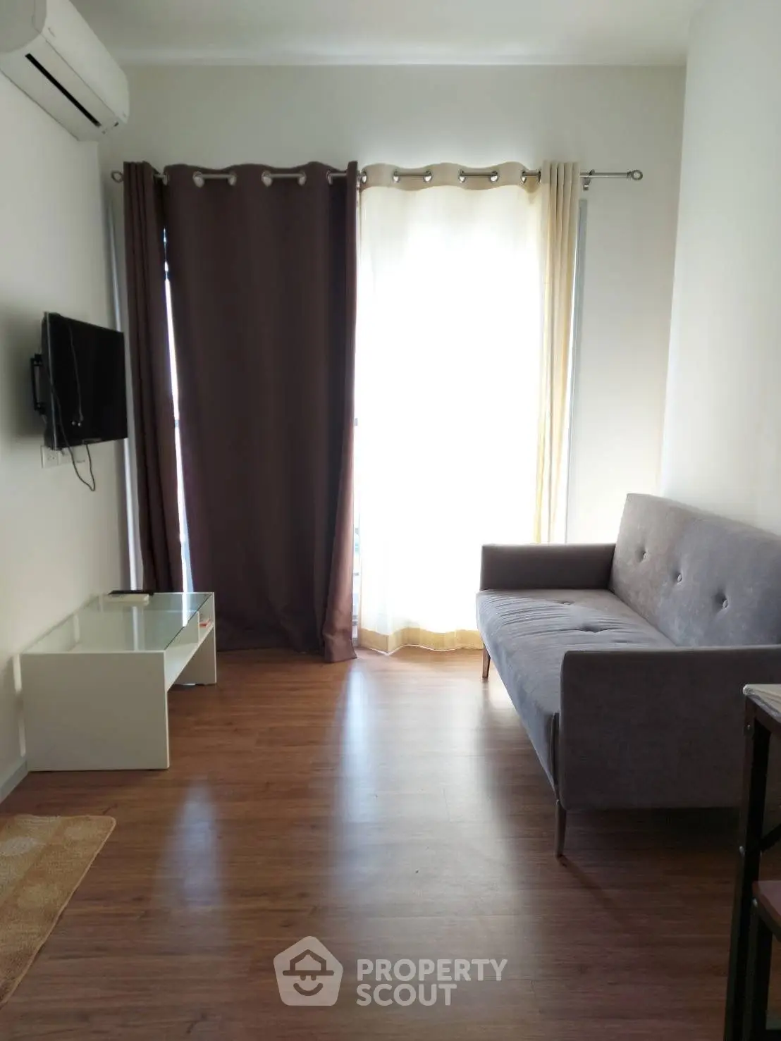 Cozy living room with modern sofa and wall-mounted TV, featuring elegant curtains and wooden flooring.