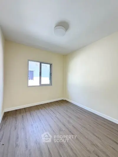 Spacious empty bedroom with wooden flooring and natural light through window.