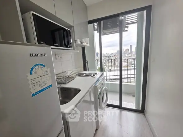 Compact kitchen with modern appliances and balcony view in urban apartment.