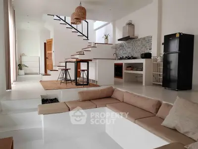 Modern open-plan living room with kitchen, featuring sleek design and cozy seating area.