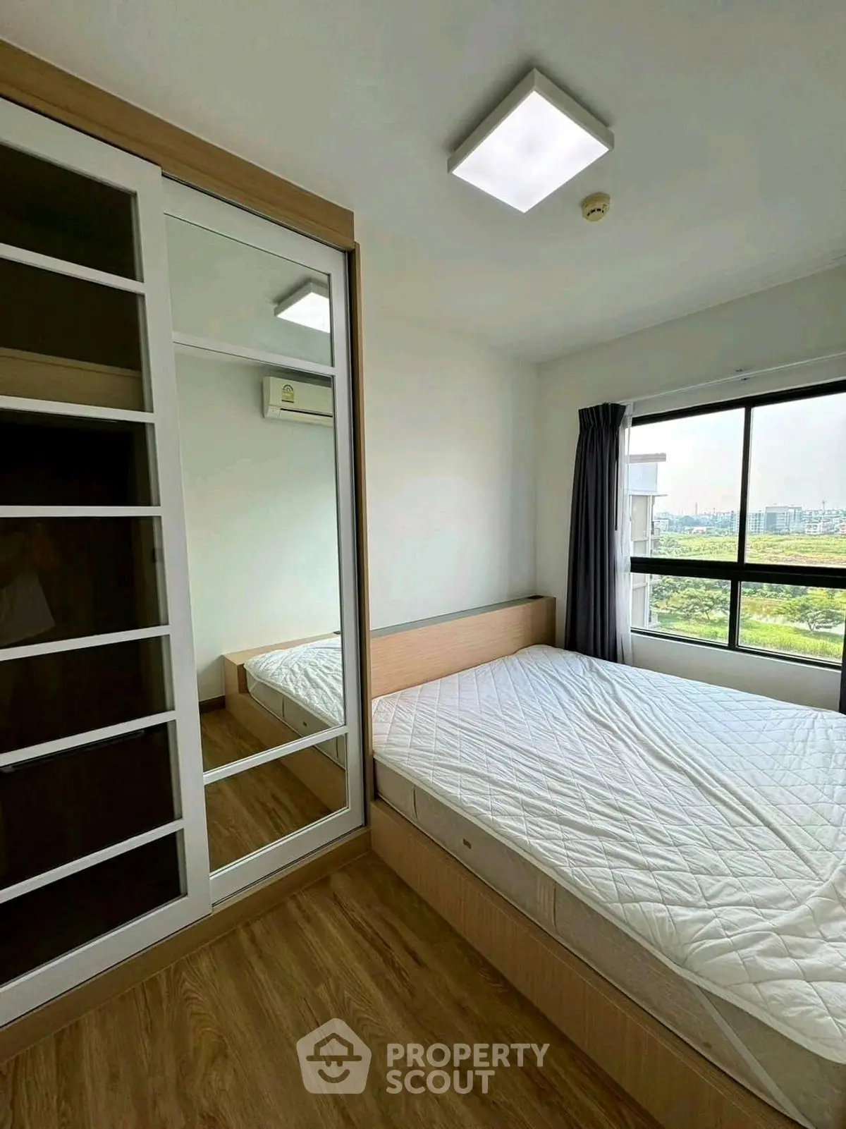 Modern bedroom with large window and mirrored wardrobe in a high-rise apartment.