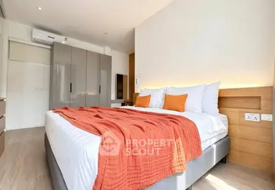 Modern bedroom with stylish decor and ample natural light, featuring a cozy bed with orange accents and sleek storage.