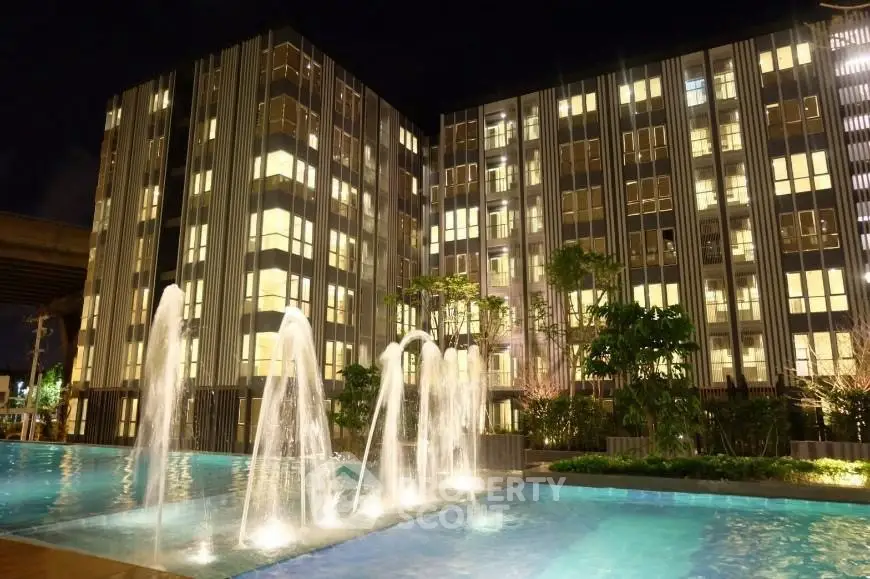 Modern apartment building with illuminated windows and elegant water fountains at night.