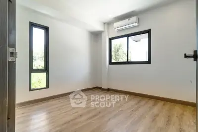 Spacious empty room with wooden flooring and large windows in modern apartment.
