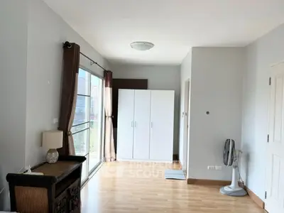 Spacious bedroom with wooden flooring and large wardrobe, featuring natural light from sliding glass doors.