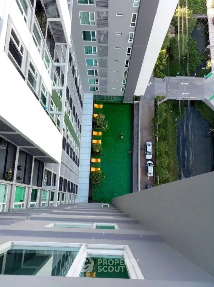 Stunning aerial view of modern apartment building with lush green courtyard and pool area.