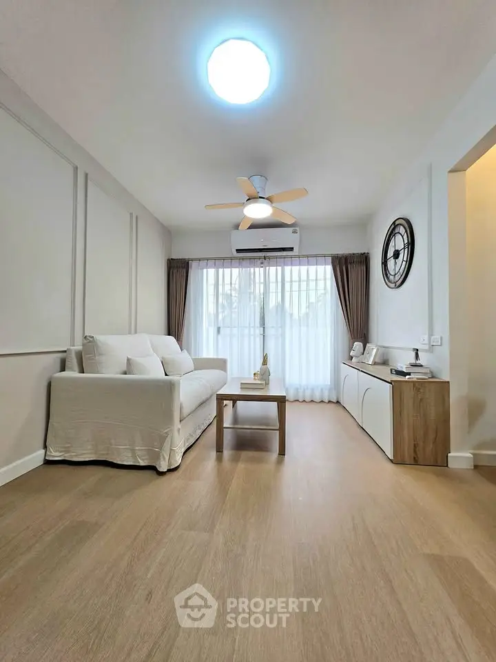 Modern living room with elegant decor, featuring a cozy sofa, stylish ceiling fan, and large window for natural light.
