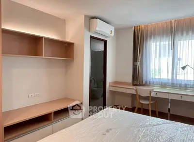 Modern bedroom with built-in shelves and desk, featuring natural light and air conditioning.