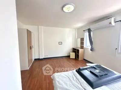 Spacious bedroom with wooden flooring and air conditioning, featuring a wardrobe and study desk.
