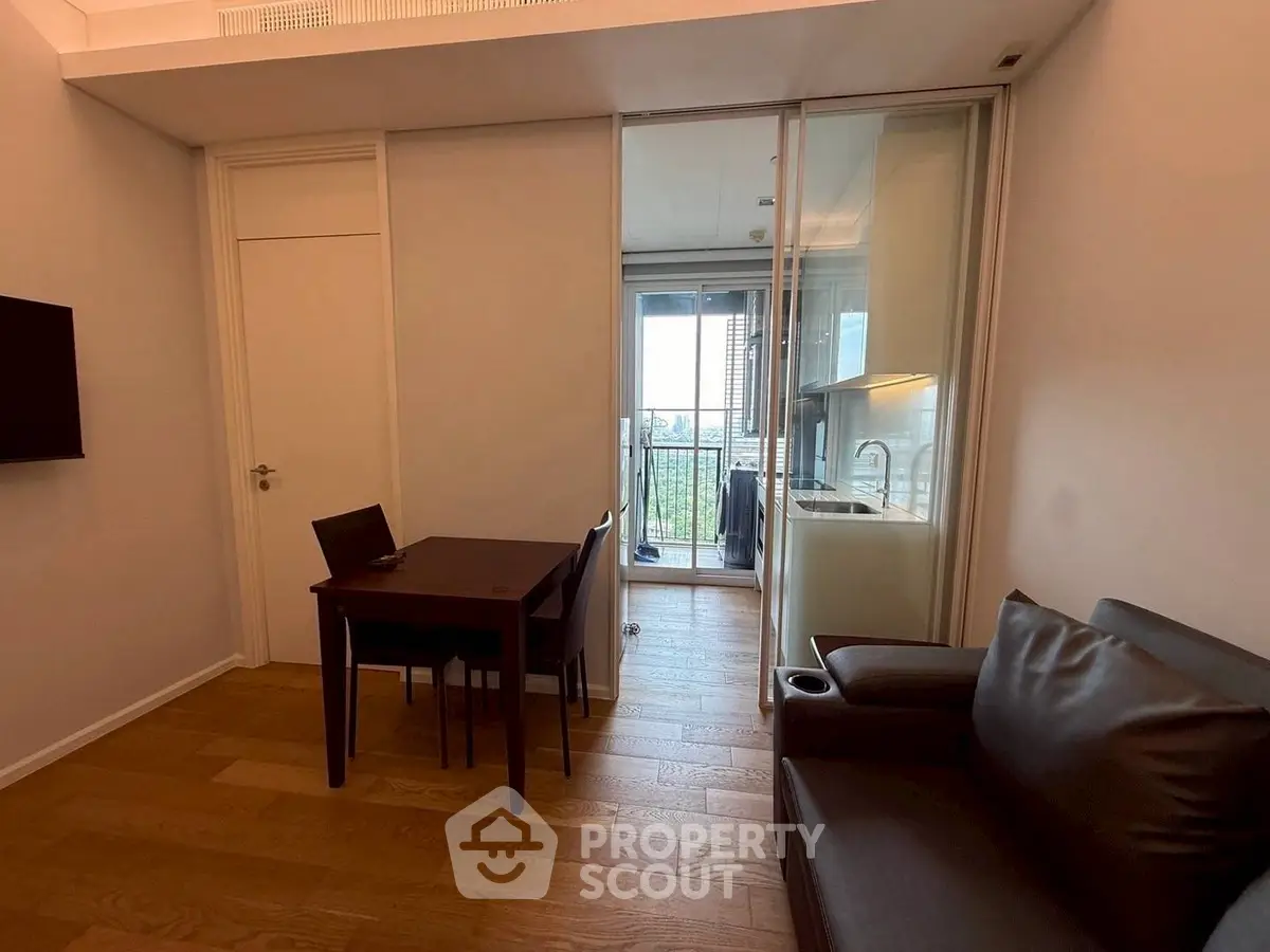 Modern living room with open kitchen and balcony view, featuring sleek furniture and wooden flooring.