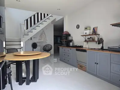 Modern kitchen with sleek cabinetry and open layout, featuring a stylish dining area and staircase.