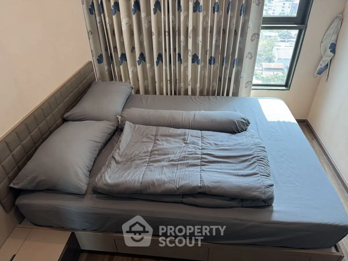 Cozy bedroom with modern decor and large window offering natural light and city view.