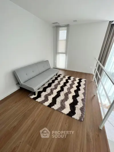 Modern minimalist living room with sleek grey sofa, patterned rug, and abundant natural light from tall windows, perfect for urban living.