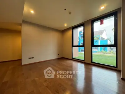 Spacious empty room with wooden flooring and large windows offering natural light.