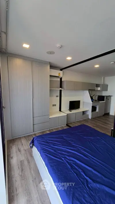 Modern bedroom with sleek built-in storage and open kitchen layout, featuring contemporary design and ample natural light.