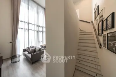 Modern duplex interior with high ceilings and elegant staircase, featuring a cozy living area with floor-to-ceiling windows.