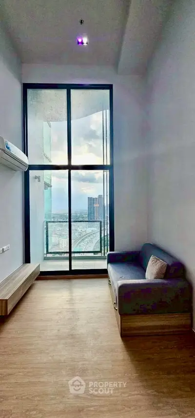 Modern living room with large window and city view, featuring a cozy sofa and wooden flooring.
