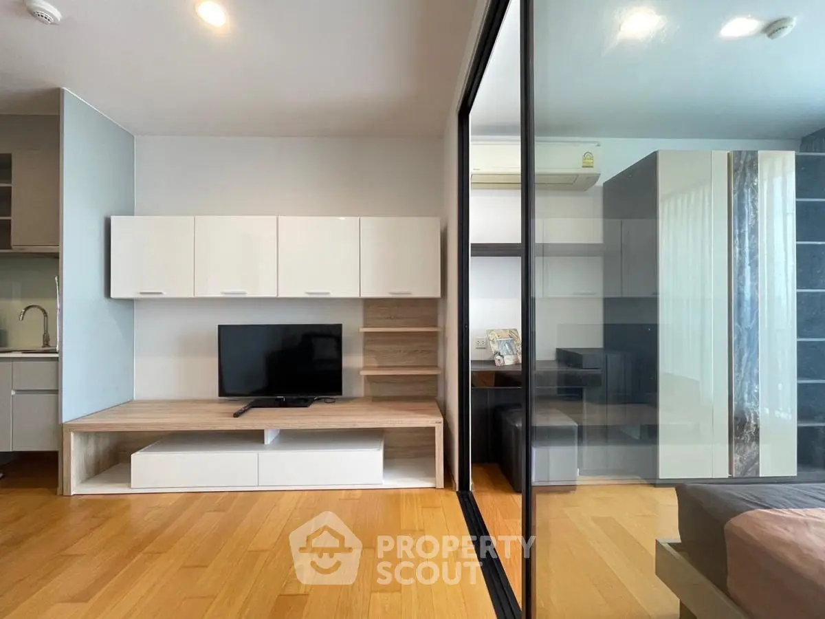 Modern living room with sleek TV unit and glass partition in stylish apartment.