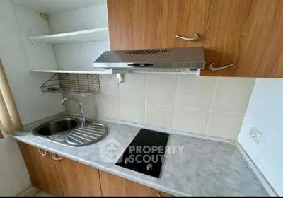 Compact kitchen with electric cooktop and stainless steel sink in modern apartment.
