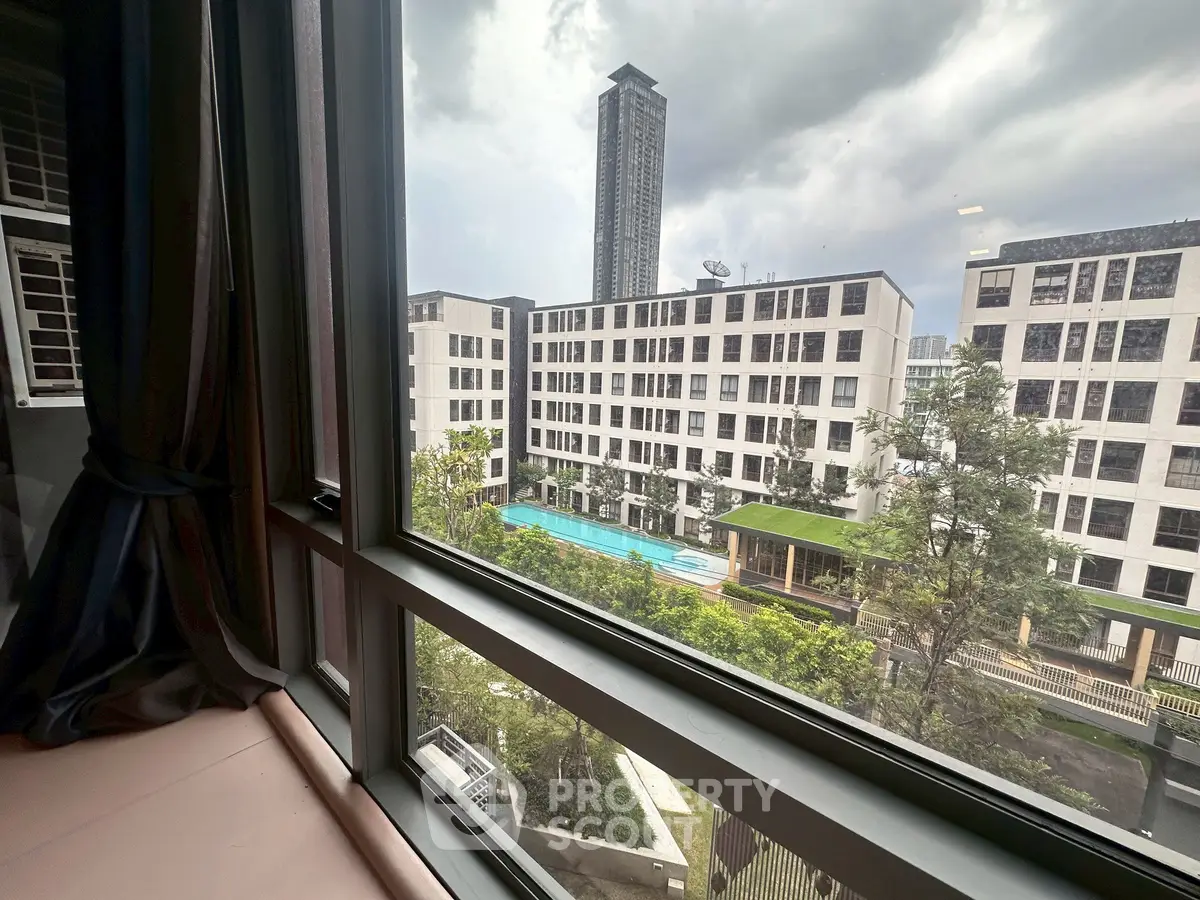 Stunning view from window overlooking modern apartment complex with pool and lush greenery.