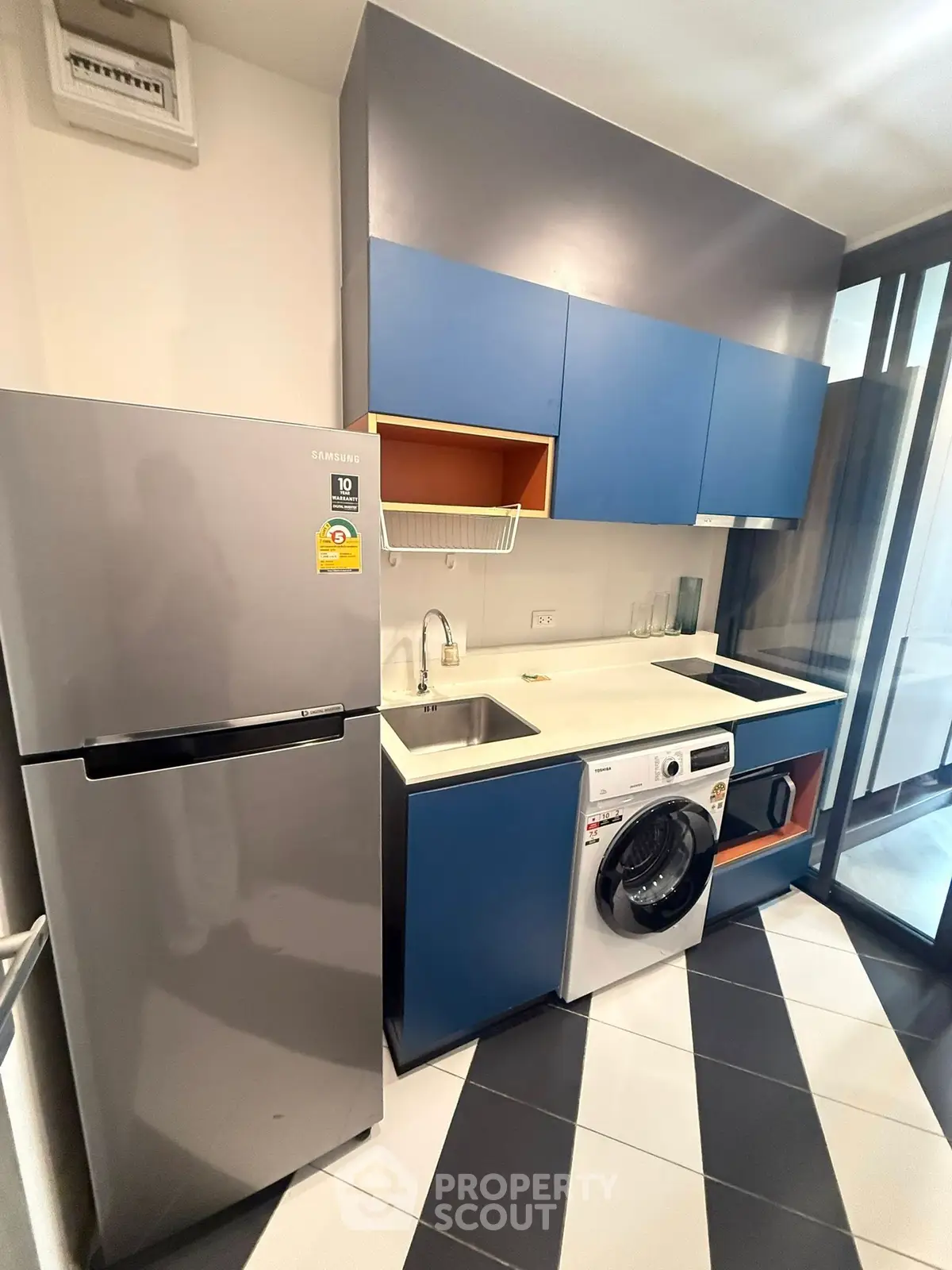 Modern kitchen with sleek cabinets, washing machine, and stainless steel fridge in compact layout.