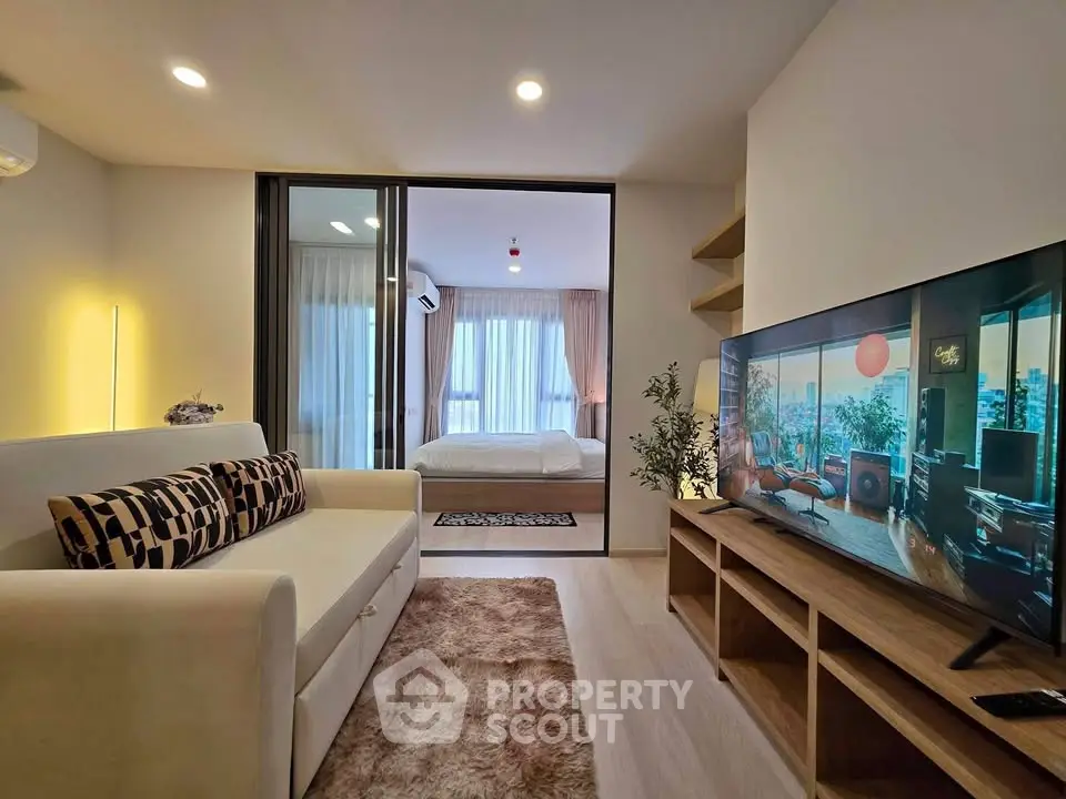 Modern living room with cozy sofa and large TV, open view to bedroom, stylish decor