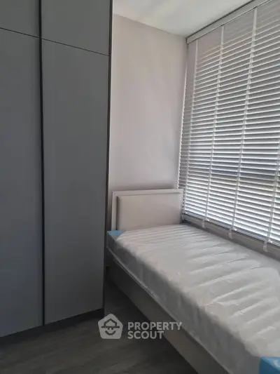 Modern minimalist bedroom with sleek wardrobe and large window blinds.