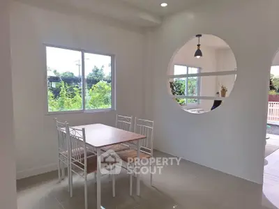Bright dining area with modern white furniture and large window overlooking greenery.