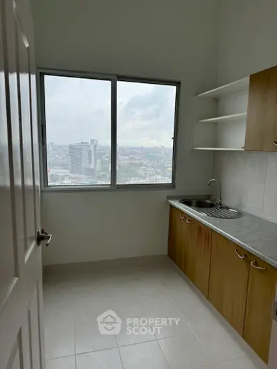 Compact kitchen with city view, featuring wooden cabinets and stainless steel sink.