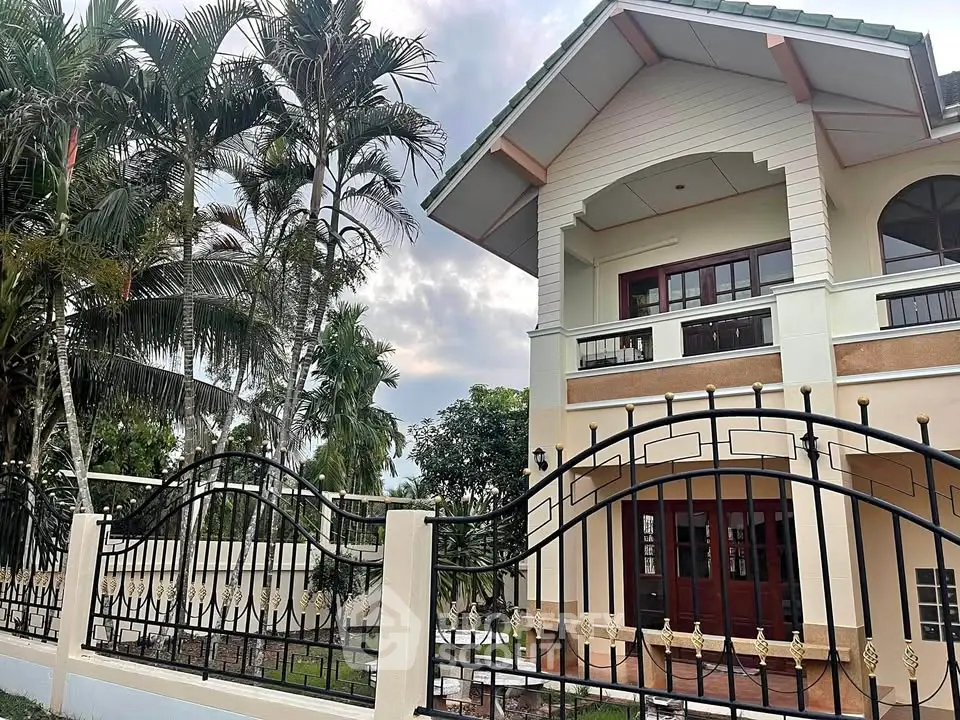 Charming two-story house with elegant iron fence and lush tropical garden, perfect for serene living.