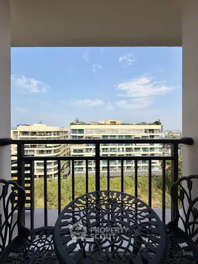 Charming balcony with elegant furniture offering a stunning view of modern buildings and clear blue sky.