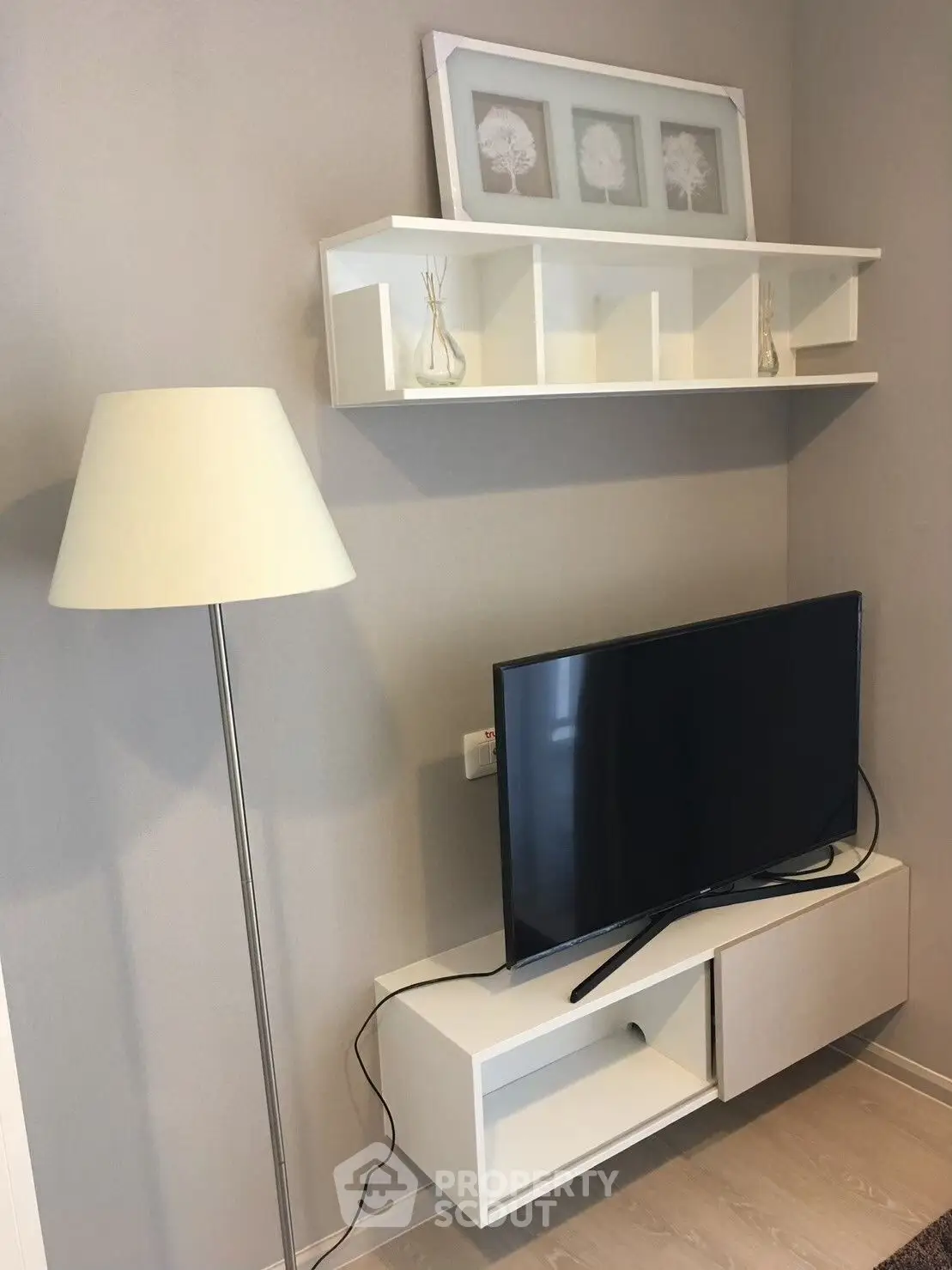 Modern living room corner with TV, stylish shelving, and floor lamp in a cozy apartment.