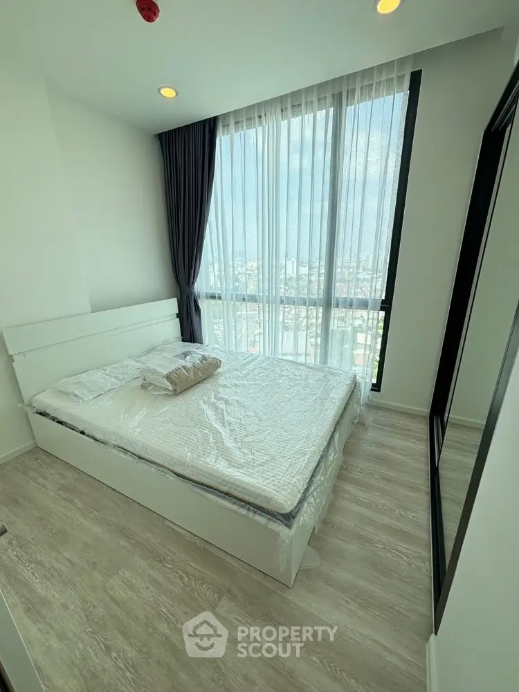 Modern bedroom with large window and city view, featuring minimalist design and natural light.