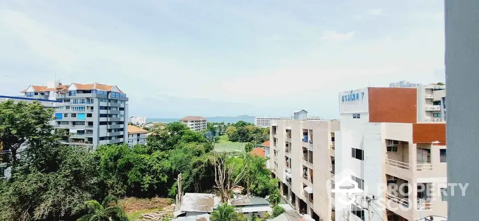 Stunning cityscape view from high-rise apartment balcony with lush greenery and distant ocean horizon.