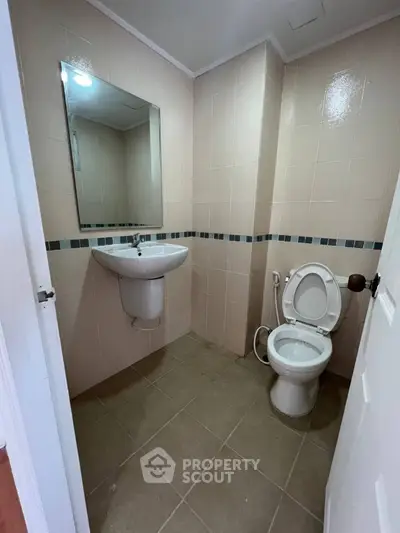 Compact bathroom with wall-mounted sink and toilet, beige tiles, and a large mirror.
