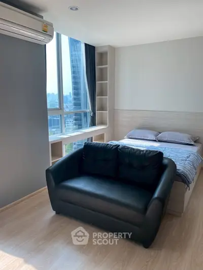 Modern studio apartment with city view, featuring a cozy black sofa and a comfortable bed.