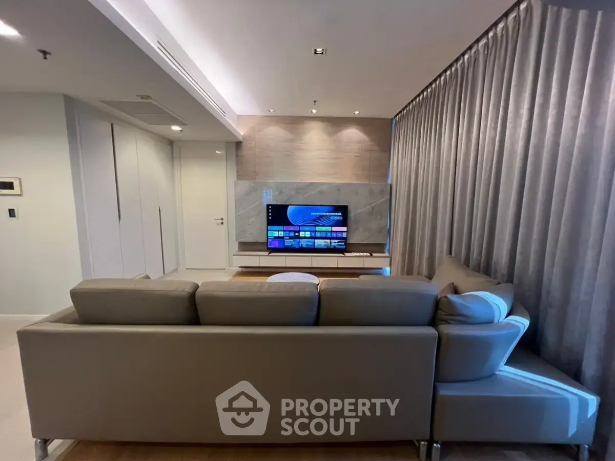 Modern living room with sleek design and large TV, featuring a comfortable sofa and elegant curtains.