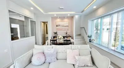 Elegant living room with modern decor and dining area, featuring large windows and stylish lighting.