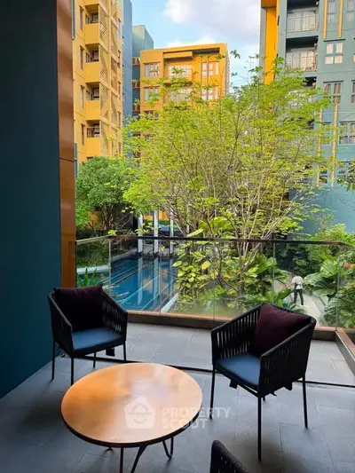 Chic balcony with modern seating overlooking lush garden and pool in vibrant urban setting.