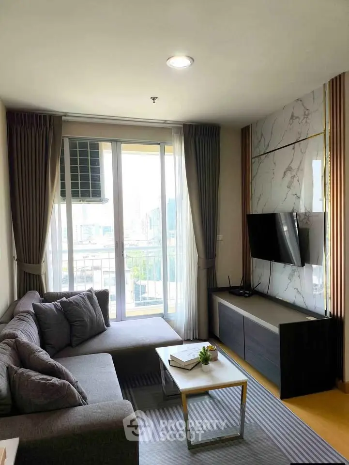 Modern living room with large windows and city view, featuring a stylish sofa and wall-mounted TV.