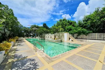 Luxurious outdoor pool area with lush greenery and clear blue sky, perfect for relaxation and leisure.